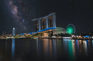 夜晚的濱海灣金沙，銀河系在上方，城市燈光倒映在水中。 — 風景動圖 壁紙