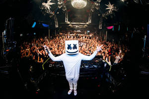DJ Marshmello 在音樂會上表演，人群歡呼，迪斯科燈光閃爍。