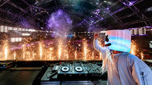DJ Marshmello 戴著發光面具在夜間節日表演，伴有煙花。