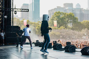 Marshmello 在節日舞台上跳舞，背景是城市天際線。