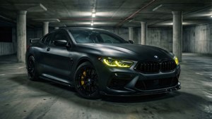 啞光黑色BMW M8 Coupe，黃色頭燈，在黑暗的混凝土車庫中。