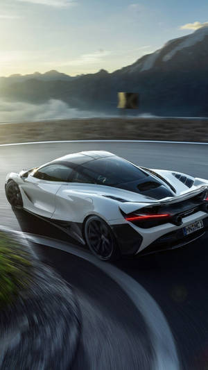 白色McLaren跑車在日落時分的山路上飛馳。