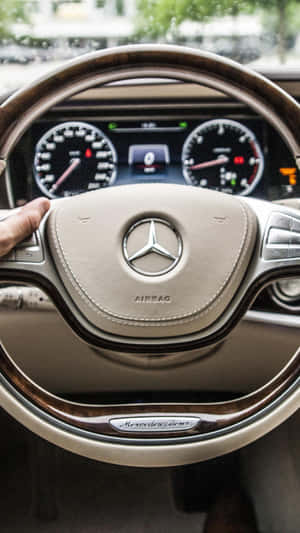 手放在 Mercedes-Benz 方向盤上，帶有木質飾邊和數位儀表板。