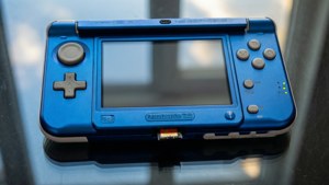 藍色 Nintendo 3DS 主機，綠色電源指示燈，置於反光玻璃表面
