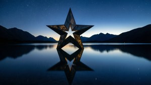 一個星形雕塑在星空下寧靜的湖面上倒映，背景有山脈。