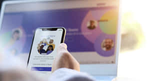 手拎住電話登入Microsoft Teams，背景有手提電腦。