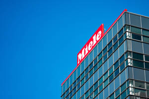 藍天下帶有紅色 Miele 標誌的現代玻璃建築