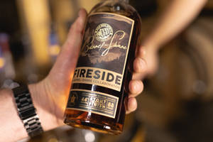 在酒吧環境中，手拿著一瓶 Fireside Barrel-Share Collaboration 黑啤威士忌。