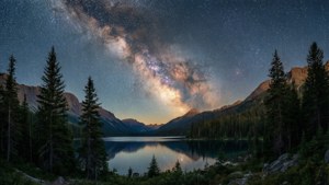 夜晚，銀河系倒映在被松樹環繞的山湖中