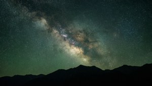 銀河系在星光照耀的夜空下在黑暗山脈上方發光