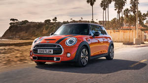 橙色MINI Cooper S在海岸道路上行駛，背景有棕櫚樹和海灘。