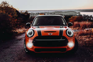 橙色MINI Cooper S停在日落時分的土路上，享有海岸景色和秋樹。