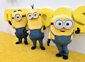 三個穿著藍色工裝褲的Minions在活動中在黃色地毯上擺姿勢。