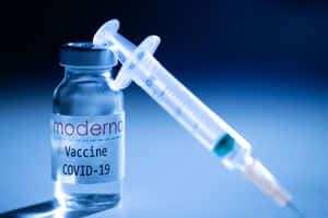 在藍色燈光下，一支注射器靠在 Moderna COVID-19 疫苗瓶上。