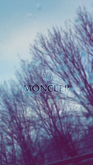 Moncler 標誌覆蓋在藍紫色調的模糊冬季樹木上。
