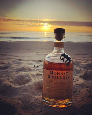 日落時沙灘上的Monkey Shoulder威士忌瓶。