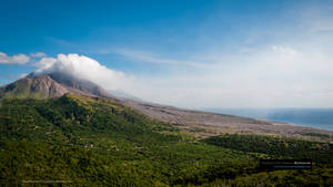 火山在藍天下向綠色山丘和海洋噴出煙霧