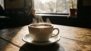陽光窗邊木桌上的冒煙咖啡杯