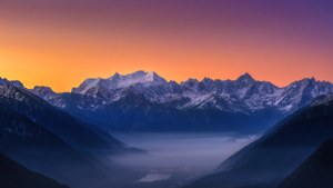 黎明時分白雪覆蓋的山脈，下方有霧氣繚繞的山谷