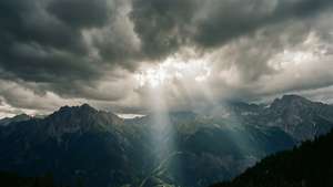 陽光穿透暴風雲，照亮崎嶇的山脈和森林覆蓋的山谷。