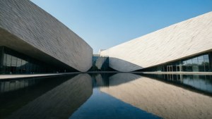 兩座現代建築，帶有波紋白色牆壁，在藍天下倒映在平靜的水池中