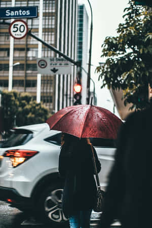 黃昏時分，一個人在雨中城市街道上拿著紅色雨傘行走。 — 雨天 壁紙