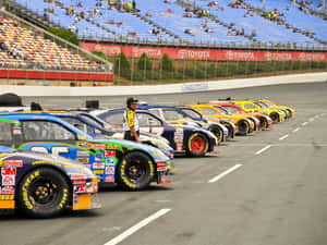 NASCAR賽車整齊排列在賽道上，旁邊站著一名安全人員。