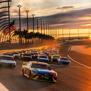 NASCAR賽車在日落時分的賽道上飛馳，背景有棕櫚樹和旗幟。