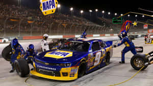 NASCAR維修站工作人員在夜間為一輛藍黃色賽車更換輪胎。