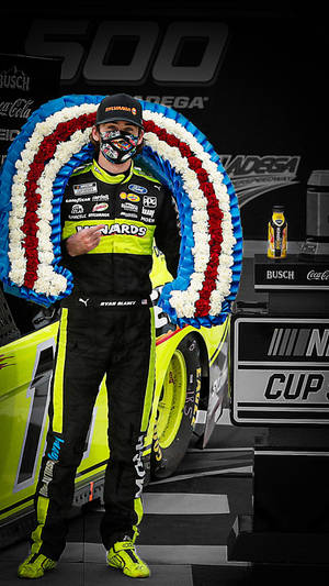 NASCAR 車手 Ryan Blaney 在賽車旁的頒獎台上手持愛國花環。