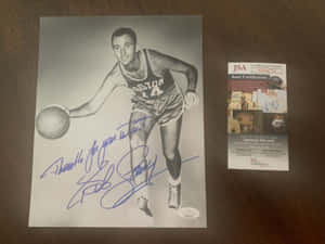 Bob Cousy身穿波士頓塞爾特人隊球衣的簽名照片，連同JSA認證卡在木桌上。 — 黑白 壁紙