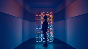 人物剪影映襯著一個發光的霓虹燈牌，上面垂直重複著名字 lucas。