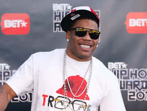 男子在BET Hip Hop Awards上戴著帽子、太陽眼鏡和珍珠項鍊微笑。 — 說唱歌手 壁紙
