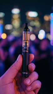 手在發光的城市背景前拿著一支黑色Puff Bar電子煙筆。