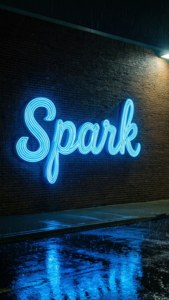 藍色霓虹燈牌寫著 Spark 在磚牆上，人行道上有雨水倒影