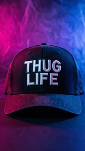 黑色卡車司機帽，在霓虹洋紅和青色燈光下帶有 'THUG LIFE' 文字