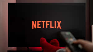 手持遙控器指向顯示 Netflix 標誌的電視在黑暗房間