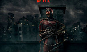 夜間，夜魔俠被鎖鏈綁在黑暗城市的屋頂煙囪上。 — Netflix GIF 壁紙