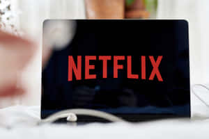 筆記型電腦顯示Netflix標誌，耳機在附近白色表面上。