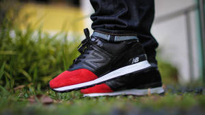 黑色和紅色 New Balance 運動鞋在草地上，搭配牛仔褲。 — 卡通鞋 壁紙