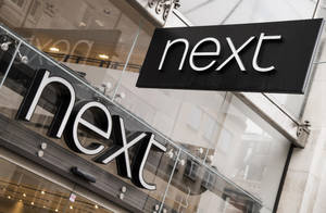 玻璃店面上的黑白「next」商店標誌，帶有城市倒影。