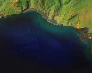 俯瞰綠色海岸線與深藍色海洋交匯，黑色火山海岸和白色浪花的航拍圖。
