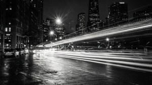 黑白夜間城市街道，帶有汽車燈光軌跡和高樓大廈
