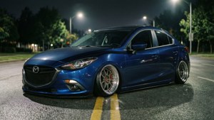 藍色Mazda 3房車配備定制輪圈停泊在夜間濕滑的街道上