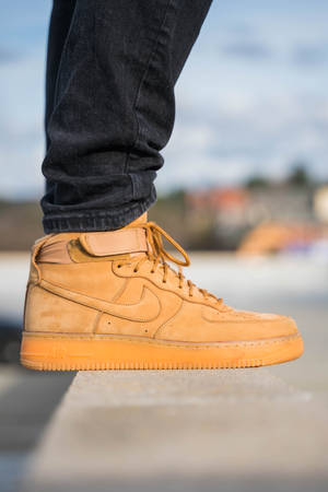 淺褐色麂皮Nike Air Force 1運動鞋與深色牛仔褲在混凝土邊緣上。