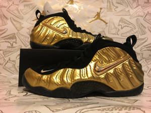 金色和黑色的Nike Air Foamposite運動鞋，背景為鞋類草圖。