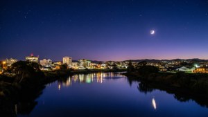 夜晚的城市天際線，月亮和星星倒映在平靜的河面上。