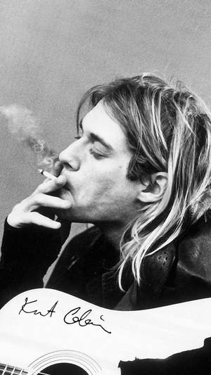 Kurt Cobain 抽煙手持簽名結他的黑白照片。