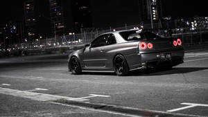 啞光灰色日產Skyline GT-R，紅色尾燈，停在夜晚城市街道。