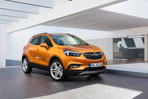 橙色Opel Mokka SUV停放在現代建築空間，玻璃牆壁，線條簡潔。